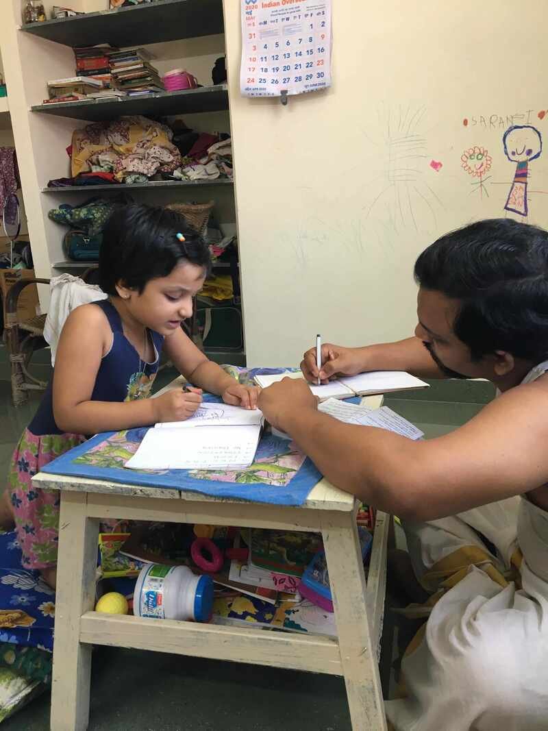 An adult and a child working together over notebooks at a small table