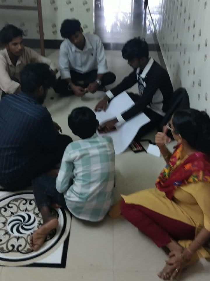 A small group sits on the floor around chart paper and crayons, working out their artwork together