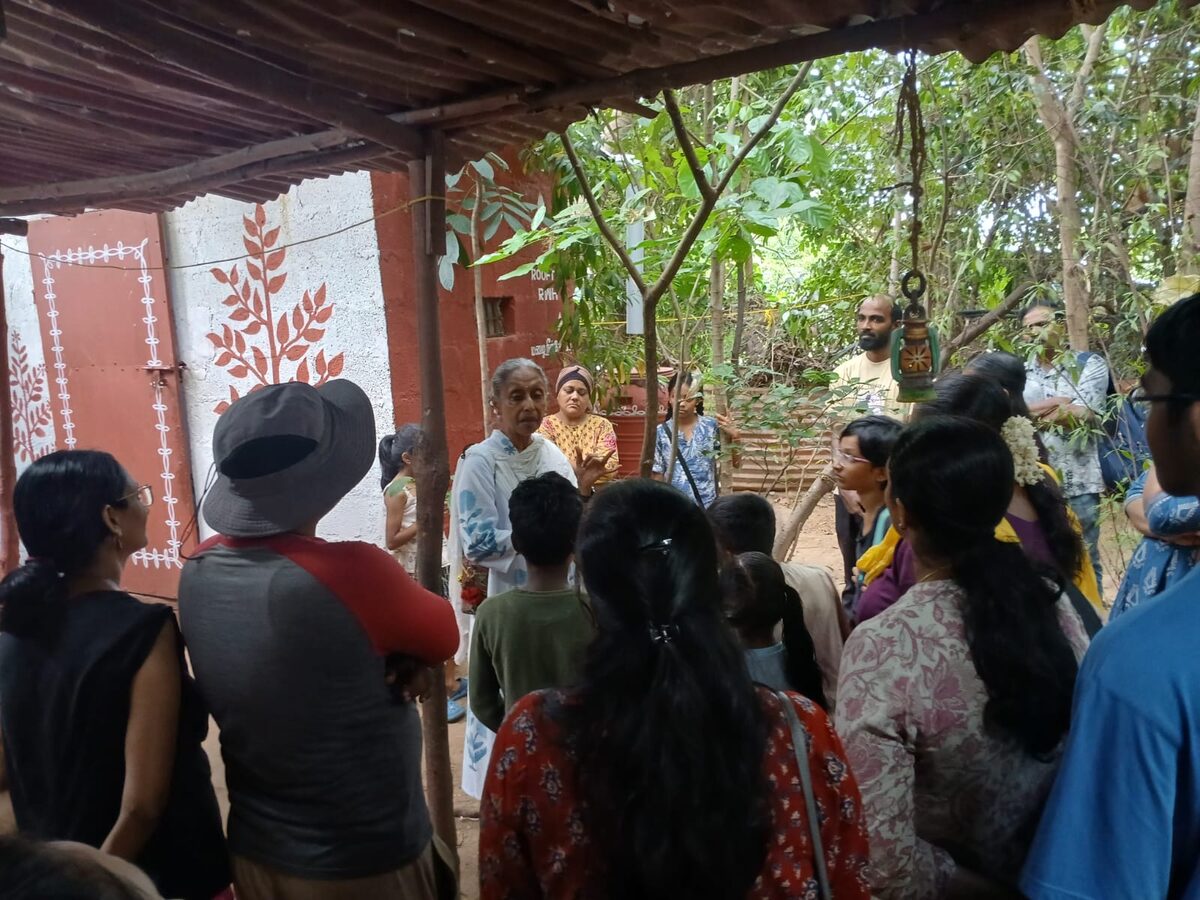 Santha Sheela Nair beginning the tour under a tiled shed, families gathered around her